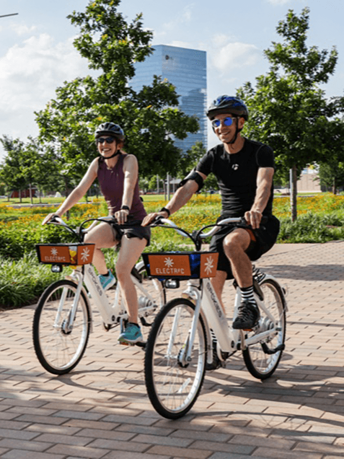 Two riders using Butterfly bike share bikes on a sunny path